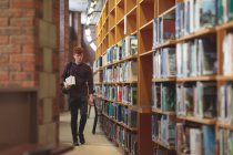 Молодой студент колледжа с книгами, идущими в библиотеке — стоковое фото