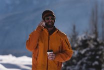 Мужчина пьет кофе, разговаривая по мобильному телефону зимой — стоковое фото