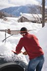 Rückansicht eines Mannes, der im Winter Schnee vom Auto fegt — Stockfoto