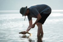 Side view of fisherman holding a fish near riverside — Stock Photo