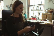 Schmuckdesignerin benutzt Handy in Werkstatt — Stockfoto