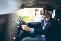 Умный бизнесмен, использующий гарнитуру виртуальной реальности за рулем автомобиля — стоковое фото