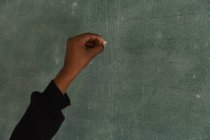 Schoolboy writing on chalkboard in classroom at school — Stock Photo
