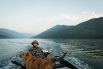 Рыбак рыбачит со своей собакой в реке в сельской местности — стоковое фото