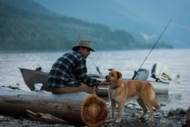 Pescatore accarezzare il suo cane vicino riva del fiume in campagna — Foto stock