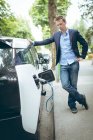 Молодой бизнесмен заряжает электромобиль на зарядной станции — стоковое фото
