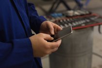 Mid section of male mechanic using mobile phone in garage — Stock Photo