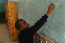 Schoolboy writing on chalkboard in classroom at school — Stock Photo