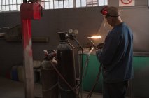 Мужской механик проверяет сварочную горелку в гараже — стоковое фото