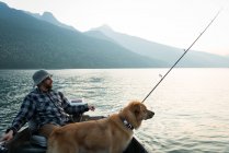 Pêcheur pêchant avec son chien dans la rivière à la campagne — Photo de stock