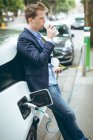 Empresário tendo café ao carregar carro elétrico na estação de carregamento — Fotografia de Stock
