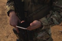 Parte média do soldado militar usando telefone celular durante o treinamento militar — Fotografia de Stock