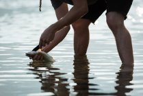 Partie médiane du pêcheur tenant un poisson près du bord de la rivière — Photo de stock
