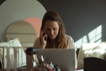 Designer di gioielli che parla sul telefono cellulare mentre utilizza il computer portatile a casa — Foto stock