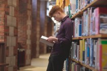 Vista laterale dello studente universitario che legge un libro in biblioteca — Foto stock