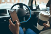 Empresária usando telefone celular enquanto toma café em um carro — Fotografia de Stock