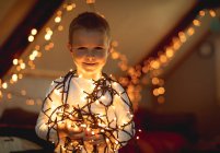 Lächelnder Junge mit beleuchteten Lichtern zu Hause — Stockfoto
