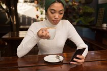 Belle femme utilisant un téléphone mobile tout en prenant un café dans le café — Photo de stock