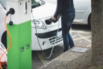 Low section of man charging electric car at charging station — Stock Photo