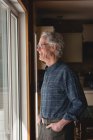 Lächelnder älterer Mann schaut zu Hause durchs Fenster — Stockfoto