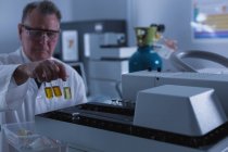 Científico masculino colocando botella química en una máquina en laboratorio - foto de stock