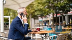 Вид збоку бізнесмена, що розмовляє на мобільному телефоні у відкритому кафе — стокове фото