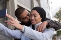 Hombre romántico besándose mujer tomando selfie en la calle de la ciudad - foto de stock