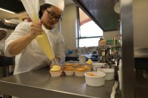 Muffins de hielo de chef hembra con bolsa de pastelería en restaurante de arte de cocina - foto de stock