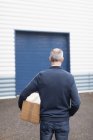 Visão traseira do entregador que transporta a parcela no armazém — Fotografia de Stock