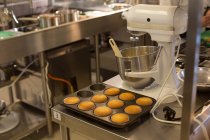 Muffins in a tray and kneading machine in kitchen — Stock Photo