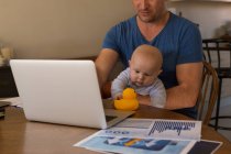 Батько використовує ноутбук, коли хлопчик грає з іграшкою вдома — стокове фото