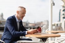 Seitenansicht eines Geschäftsmannes, der sein Handy im Outdoor-Café benutzt — Stockfoto