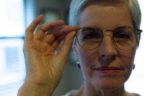 Primo piano donna anziana guardando la fotocamera mentre tiene gli occhiali in clinica — Foto stock