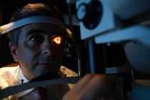 Оптометрист осматривает глаза пациентов с щелевой лампой в клинике — стоковое фото