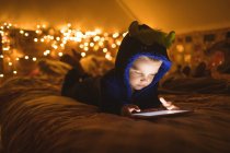 Garçon concentré en veste bleue en utilisant une tablette numérique contre les lumières de Noël — Photo de stock