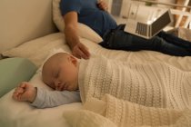 Baby boy sleeping while father using laptop in bedroom at home — Stock Photo