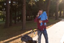 Père parlant sur un téléphone portable tout en tenant son petit garçon dans le parc — Photo de stock