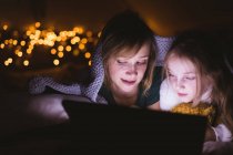 Primer plano de madre e hija usando tableta digital contra luces navideñas - foto de stock