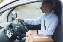 Side view of delivery man with package driving a delivery van — Stock Photo