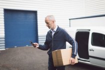 Uomo di consegna utilizzando il telefono cellulare al magazzino — Foto stock