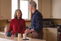 Старша пара взаємодіє один з одним, маючи каву на кухні — стокове фото