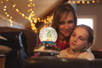 Mother and daughter looking at Christmas tree snow globe at home — Stock Photo