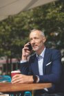 Бизнесмен разговаривает по мобильному телефону в кафе на открытом воздухе в солнечный день — стоковое фото