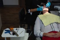Odontóloga examinando a una paciente con herramientas en clínica dental - foto de stock