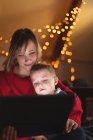 Крупним планом мати і син використовують цифровий планшет з різдвяними вогнями на задньому плані — стокове фото