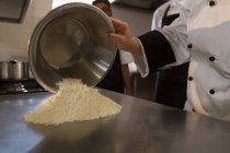 Sección media del chef femenino vertiendo harina en la encimera en la cocina - foto de stock