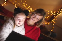 Madre e hija usando tableta digital en casa durante la Navidad - foto de stock