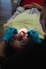 Odontóloga examinando a una paciente con herramientas en clínica dental - foto de stock