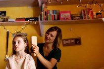 Усміхнена мати розчісує дочки волосся вдома — стокове фото