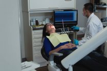 Dentista masculino usando PC de escritorio mientras examina a una paciente en la clínica - foto de stock